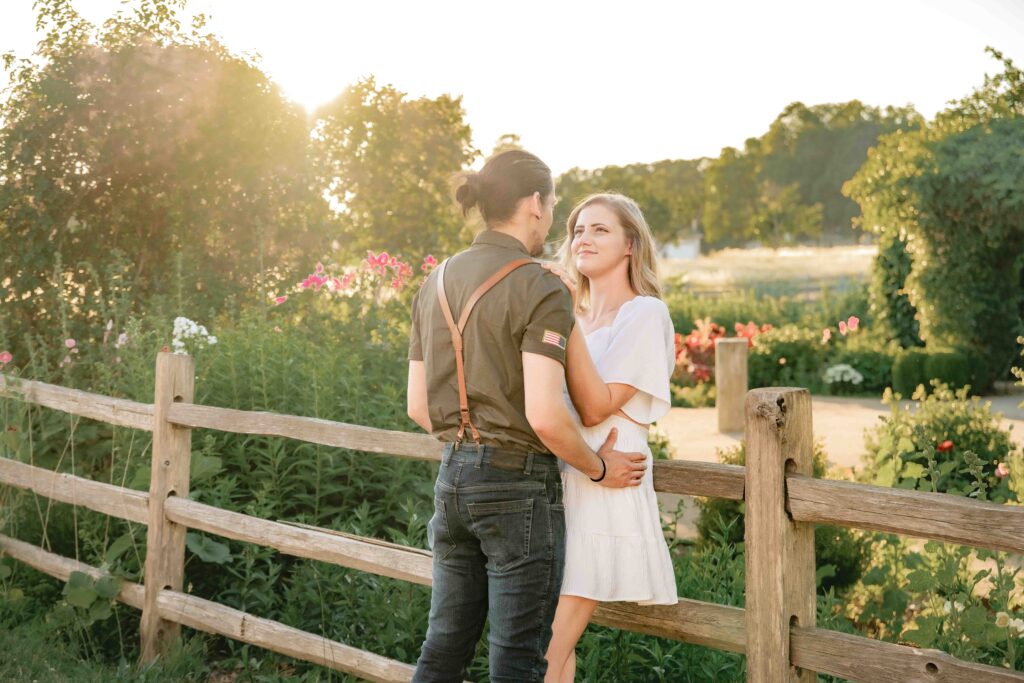 engaged couple standing along a fence at Fort Vancouver in golden hour sunlight