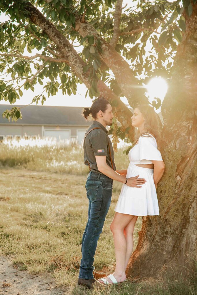 Engaged couple leaning against a tree in the golden hour sunlight at Fort Vancouver, WA